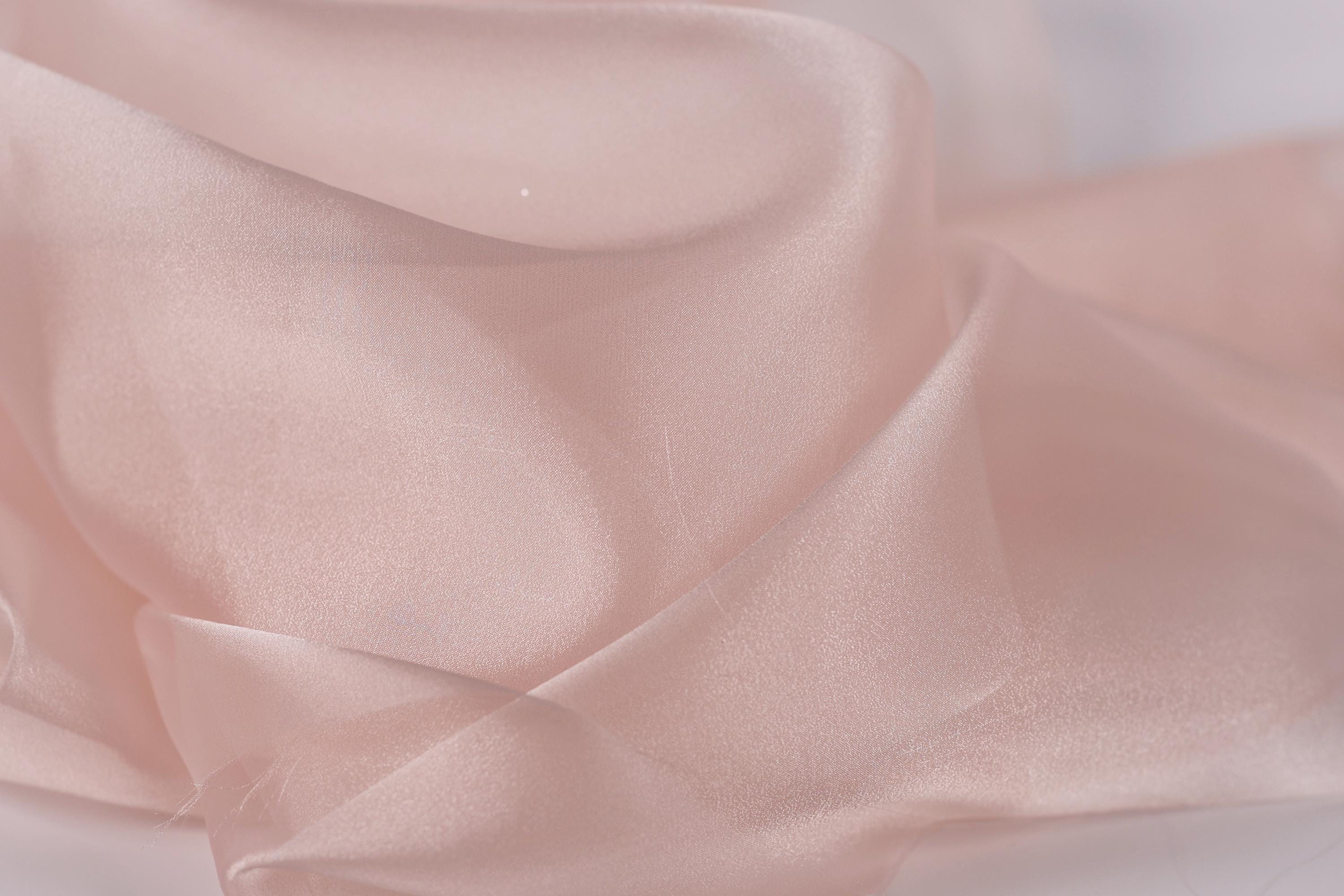 A close-up view of a soft, light pink fabric, possibly silk or chiffon, with a slightly wrinkled texture.