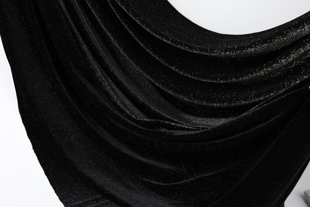 The image is a close-up of a shiny black fabric with a sparkling texture, creating a visually striking contrast against the white background.