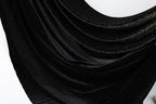 The image is a close-up of a shiny black fabric with a sparkling texture, creating a visually striking contrast against the white background.