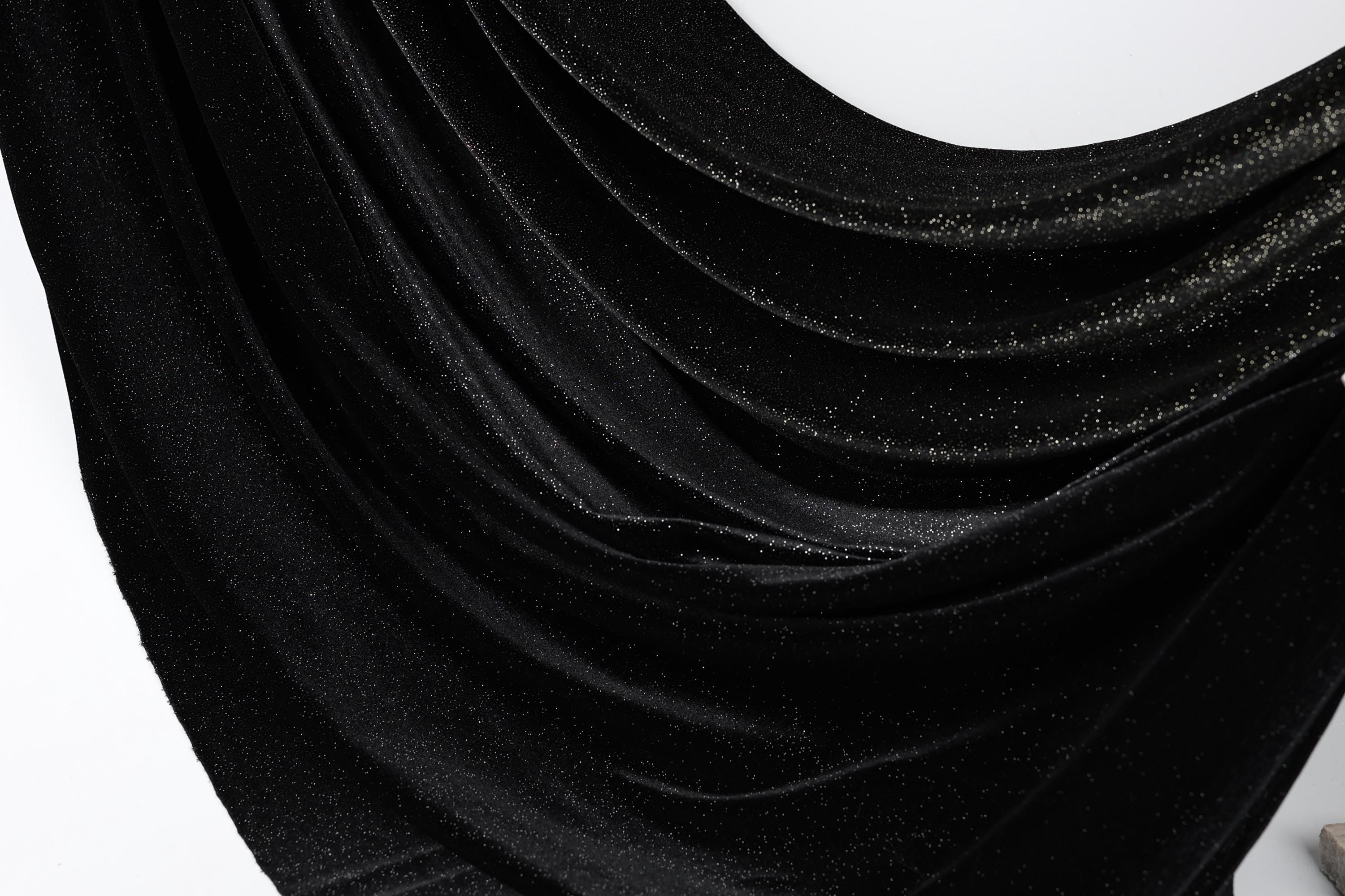 The image is a close-up of a shiny black fabric with a sparkling texture, creating a visually striking contrast against the white background.