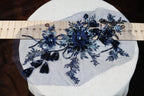 a close-up view of a piece of fabric with a floral design, including blue and black sequins and tassels. The fabric is placed on a white surface, and a ruler is visible in the background.
