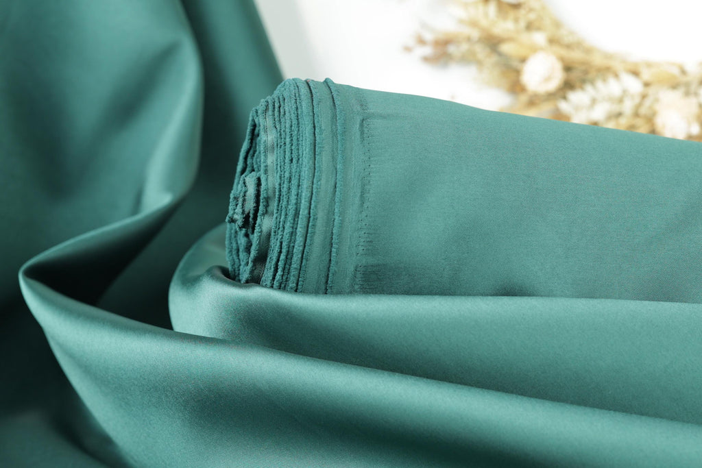 A close-up view of a piece of green fabric, possibly silk or satin, with a blurred floral background.