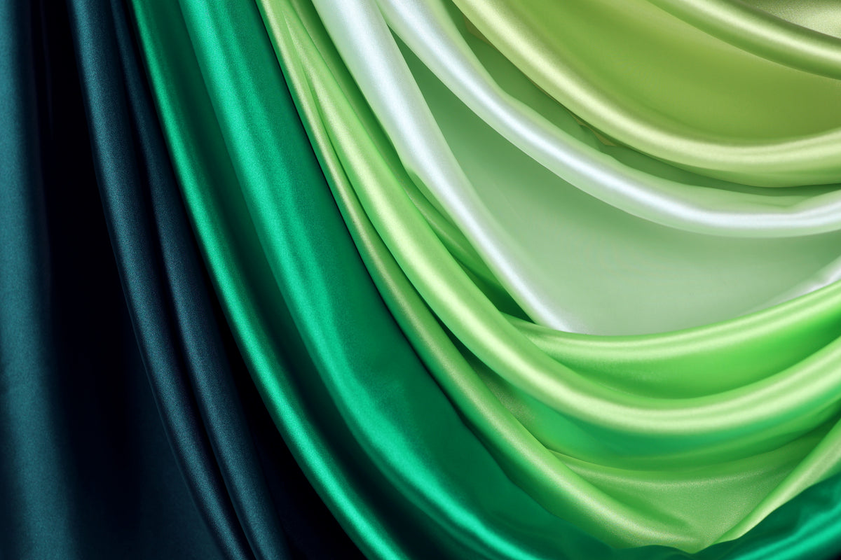 a close-up view of a collection of colorful satin fabric, with a gradient of green and blue hues. The fabric appears to be folded or draped in a way that creates a visually striking and textured effect.