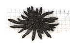 a close-up view of a black, spiky object with numerous small, shiny beads or sequins attached to it. The object appears to be a decorative piece, possibly a piece of jewelry or a textile. The object is placed on a ruler, which is positioned on a white surface.