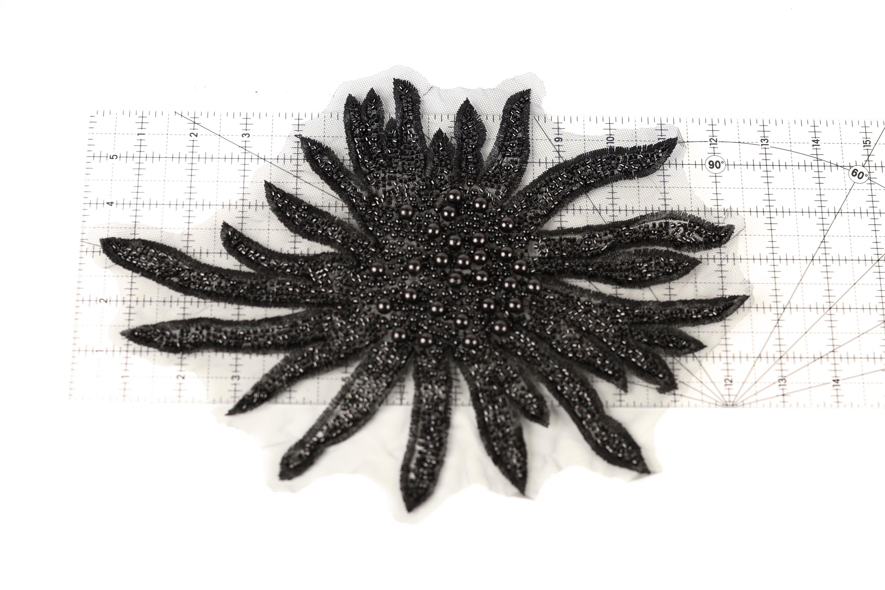 a close-up view of a black, spiky object with numerous small, shiny beads or sequins attached to it. The object appears to be a decorative piece, possibly a piece of jewelry or a textile. The object is placed on a ruler, which is positioned on a white surface.