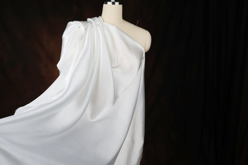 A mannequin wearing a white, flowing garment against a dark background.