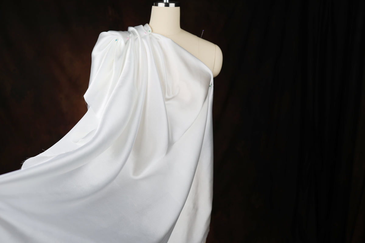A mannequin wearing a white, flowing garment against a dark background.