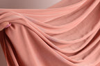 A close-up view of a soft, flowing pink fabric, possibly a sheer or sheer-like material, being held in someone's hand.
