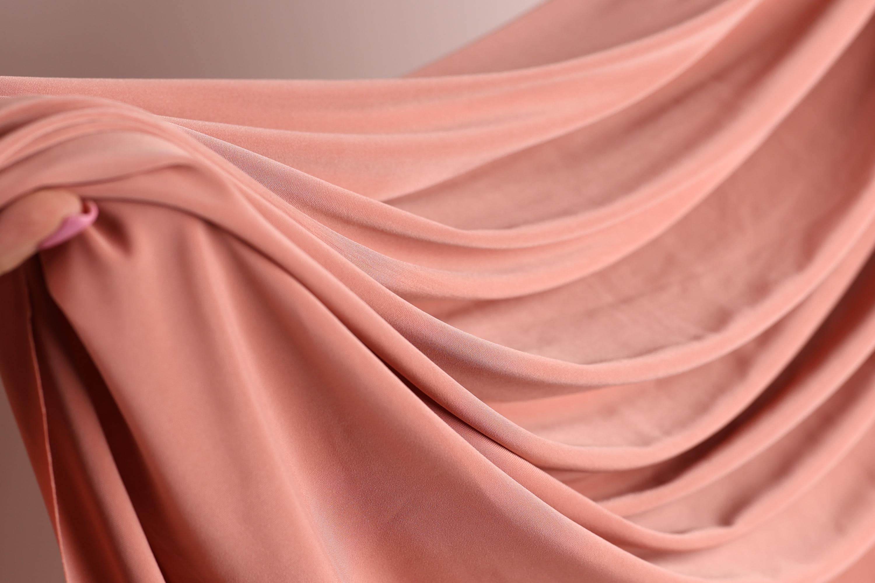 A close-up view of a soft, flowing pink fabric, possibly a sheer or sheer-like material, being held in someone's hand.
