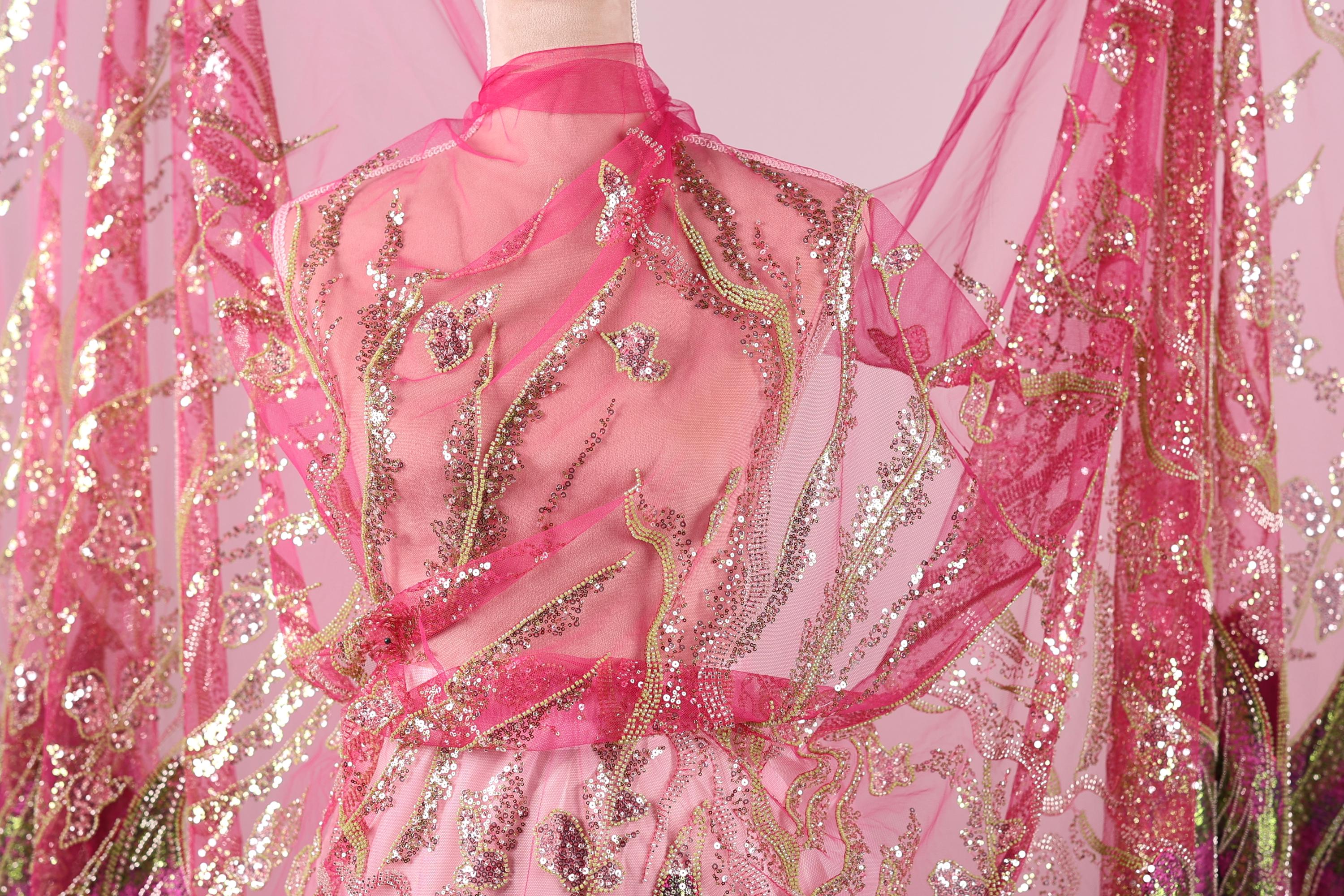 A mannequin wearing a pink and gold sequined dress with a sheer pink and gold fabric draped over it.
