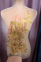 A hand holding a gold-colored, intricately designed fabric with floral and leaf-like patterns.