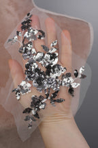 A hand holding a piece of white fabric with black and silver sequin designs.