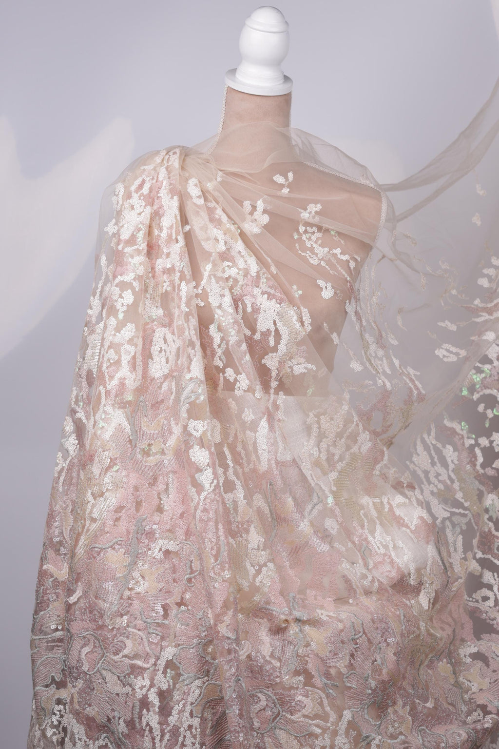 A close-up view of a delicate, lace-like fabric with a floral pattern, featuring a white and pink color scheme.