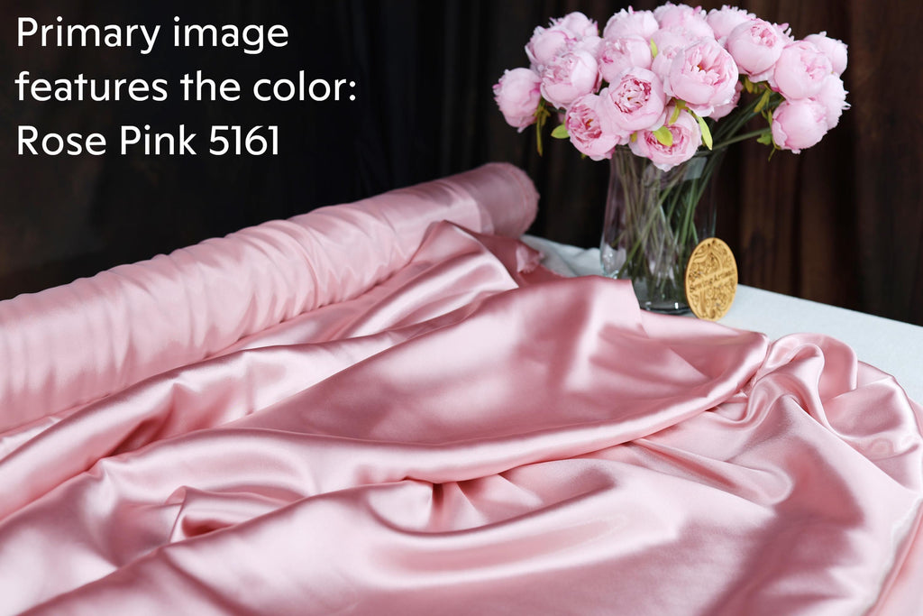 a pink satin fabric, a vase of pink peonies, and a roll of pink satin fabric on a table.
