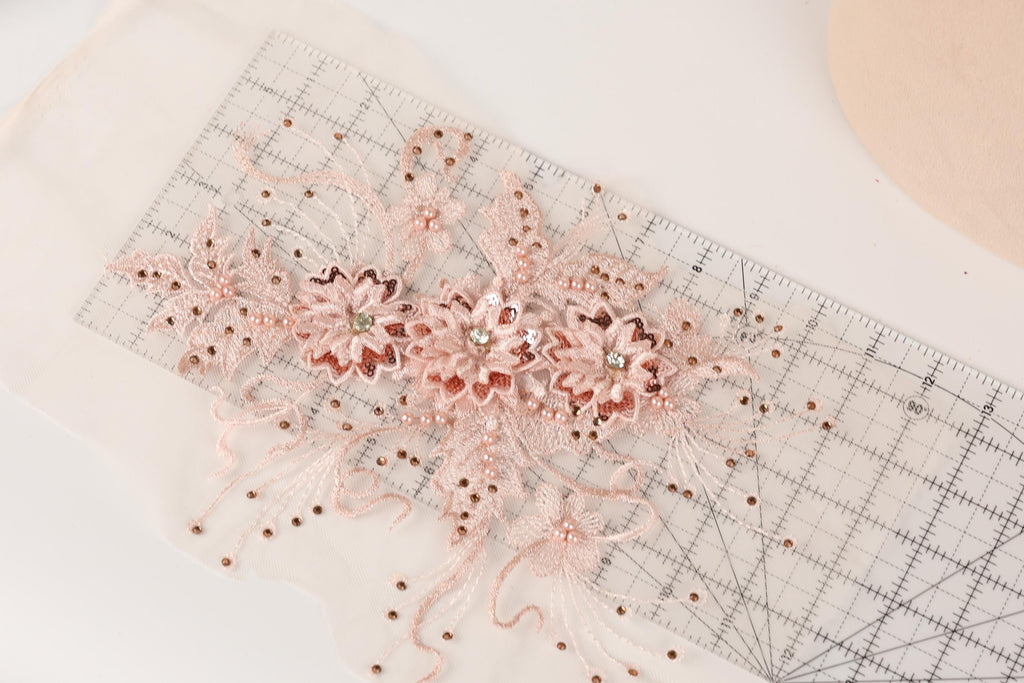 a close-up view of a delicate, intricate piece of lace or fabric adorned with small, sparkling beads or sequins. The lace appears to be embellished with a floral design, adding a touch of elegance and sophistication to the piece. The image is a close-up of the lace, showcasing its intricate details and craftsmanship.