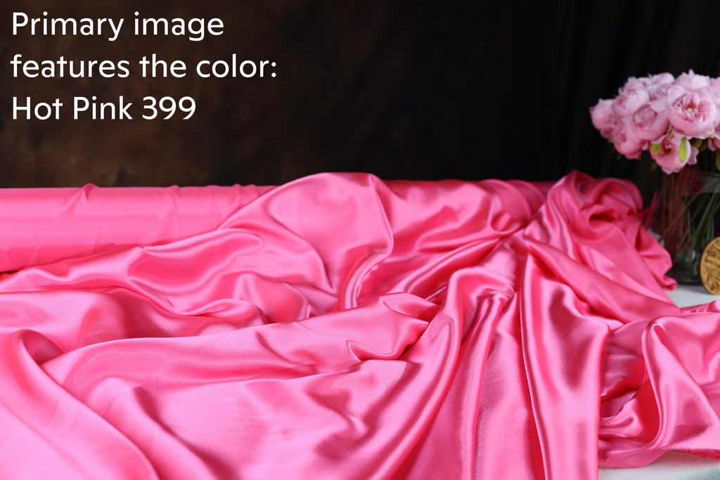 a close-up view of a crumpled, shiny pink satin fabric, with a vase of pink flowers visible in the background.