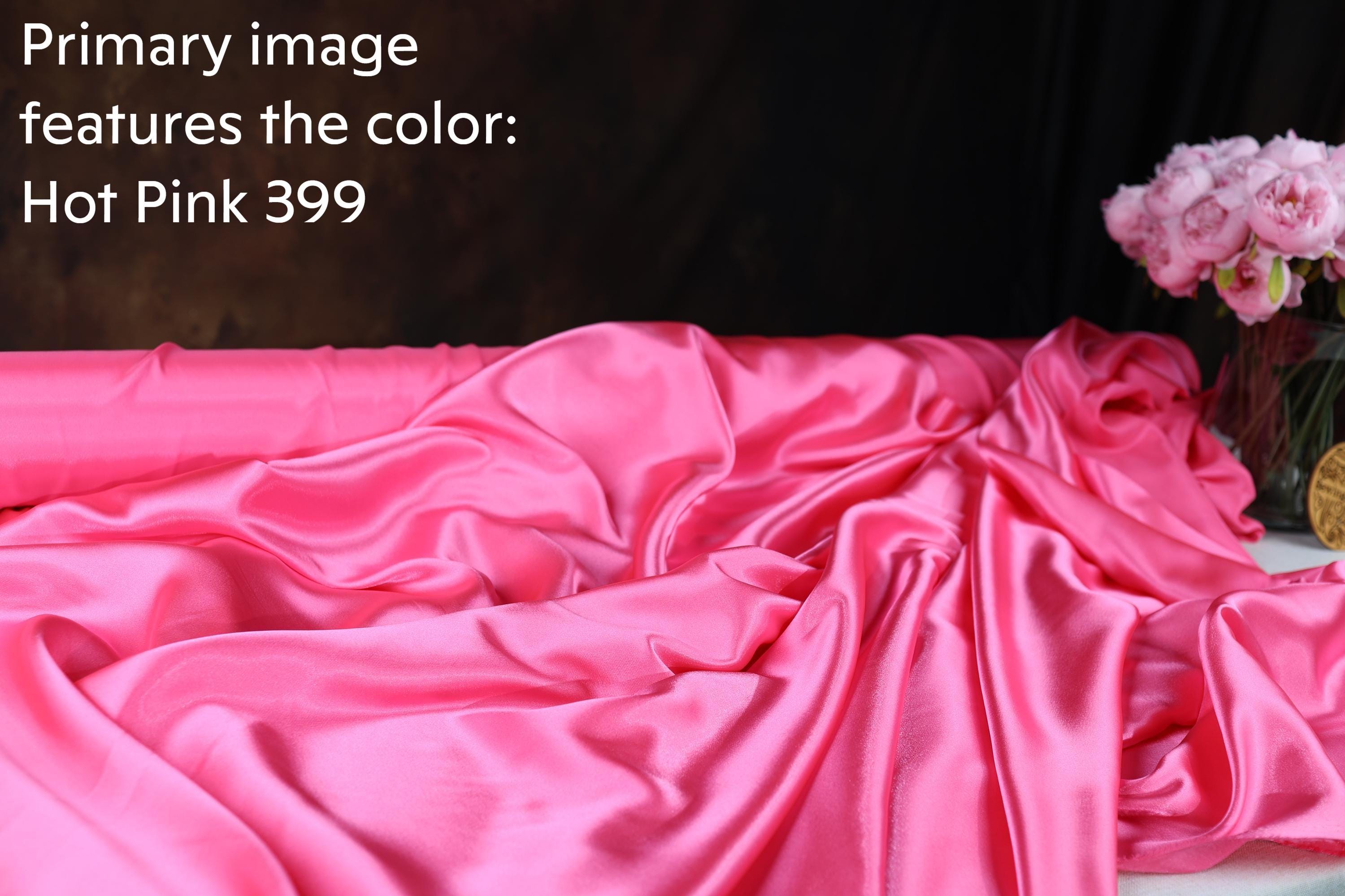 a close-up view of a crumpled, shiny pink satin fabric, with a vase of pink flowers visible in the background.