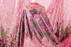 a vibrant, intricately designed fabric with a mix of pink, green, and gold colors. The fabric appears to be a sheer or sheer-like material, with a pattern of leaves and flowers that adds a touch of nature to the design. The fabric is displayed in a way that showcases its details and patterns, making it an eye-catching and visually appealing piece.