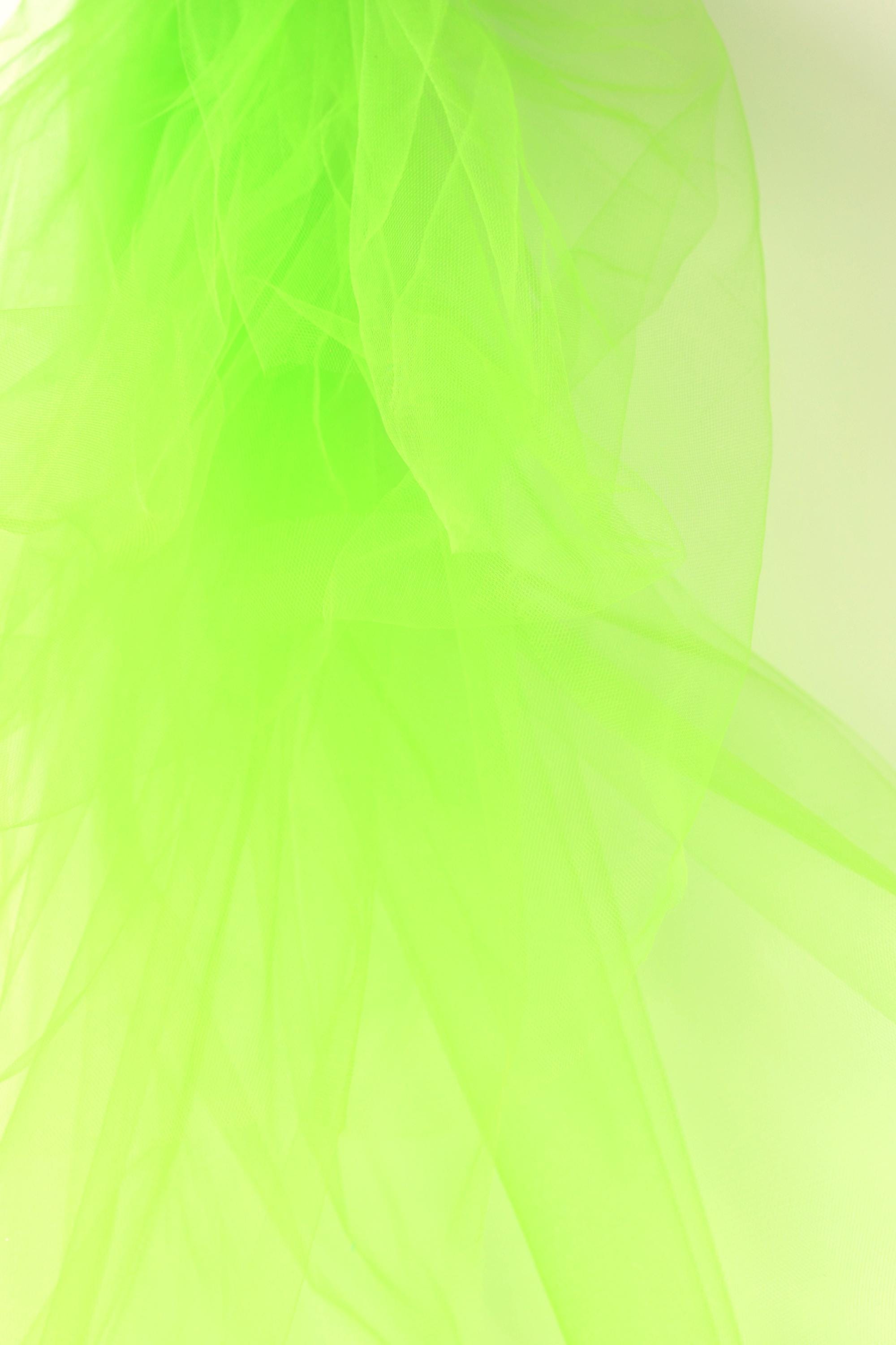 The image is a close-up of a green, translucent material, possibly a type of fabric or paper, with a soft, flowing texture. The color is bright and vibrant, creating a visually striking contrast against the light background.