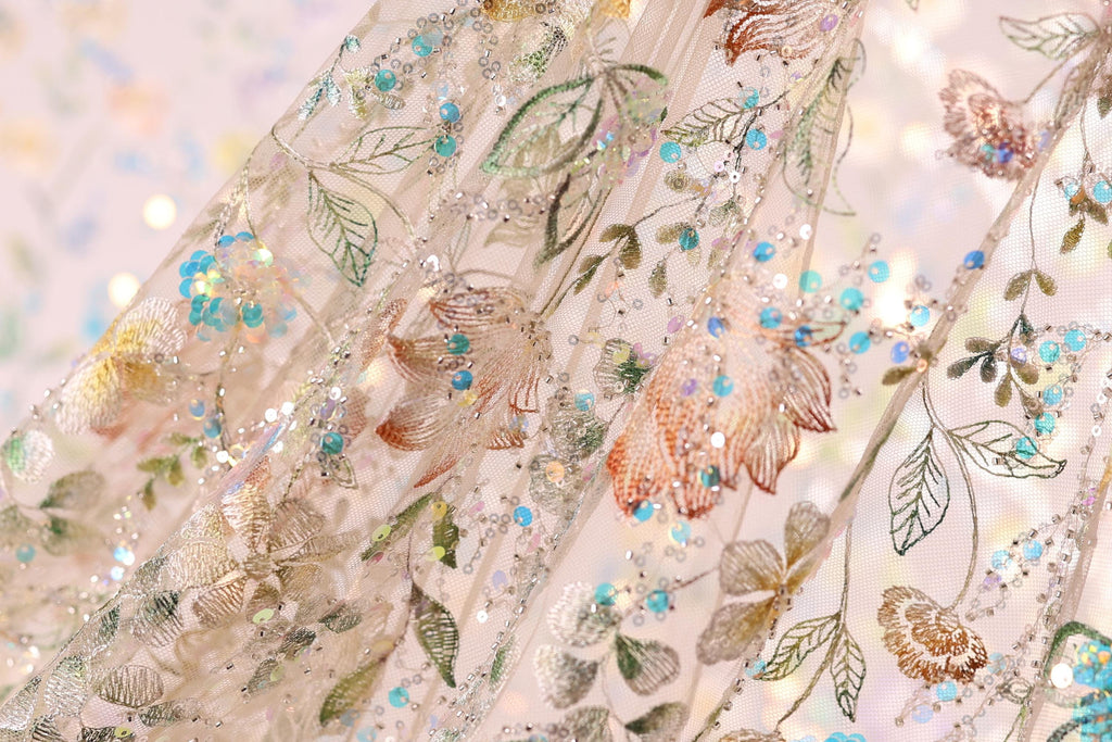 The image is a close-up of a delicate, intricately embroidered fabric with a floral pattern. The fabric is adorned with small, colorful beads and sequins that add a touch of sparkle and elegance to the design. The close-up view allows for a detailed examination of the fabric's texture and the intricate patterns created by the embroidery.