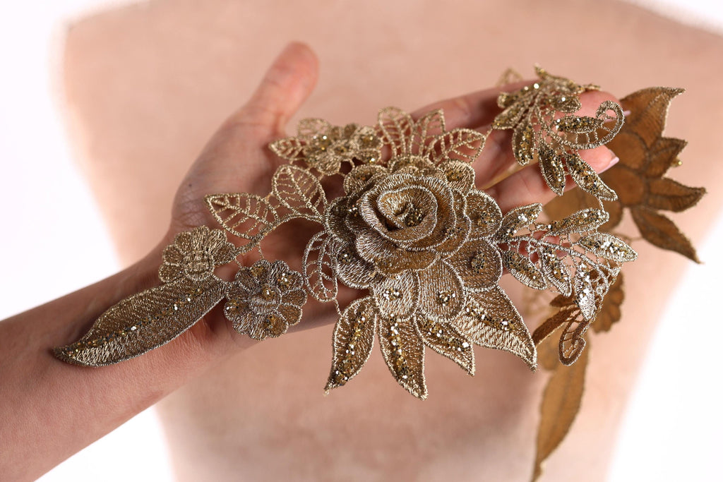 A hand holding a decorative piece of gold embroidered fabric with intricate floral designs.