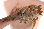 A hand holding a decorative piece of gold embroidered fabric with intricate floral designs.