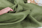 A hand is holding a piece of green fabric, which appears to be made of linen.