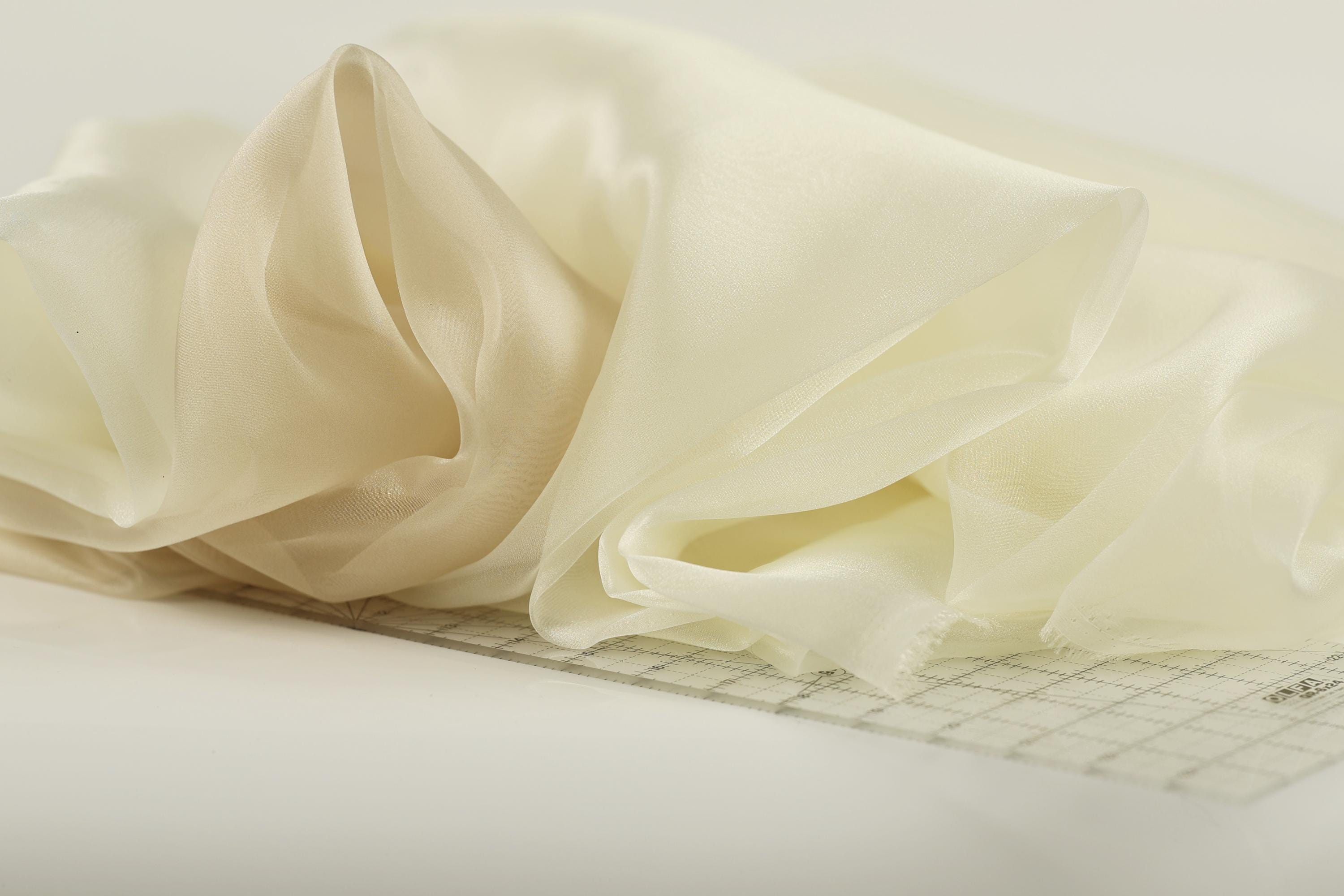 a close-up view of a piece of fabric, possibly a sheer or sheer-like material, with a grid pattern on it. The fabric appears to be folded or rolled, and it is resting on a surface, possibly a table or a cutting mat.