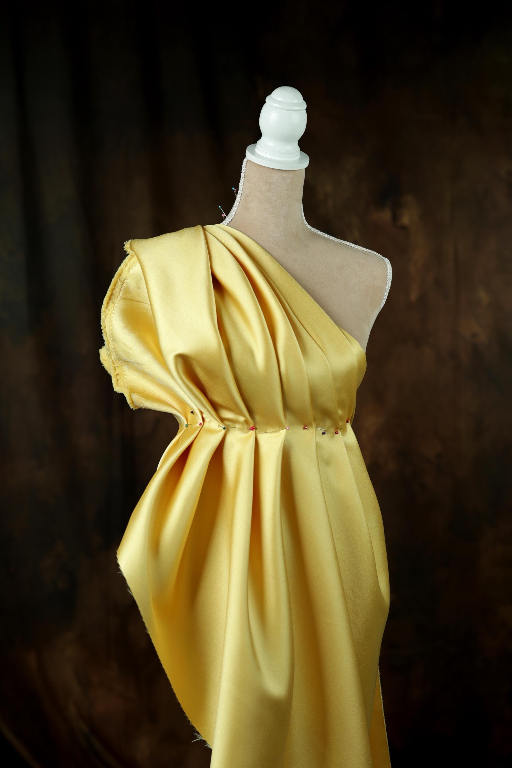 A mannequin wearing a yellow one-shoulder dress with a draped, flowing silhouette.