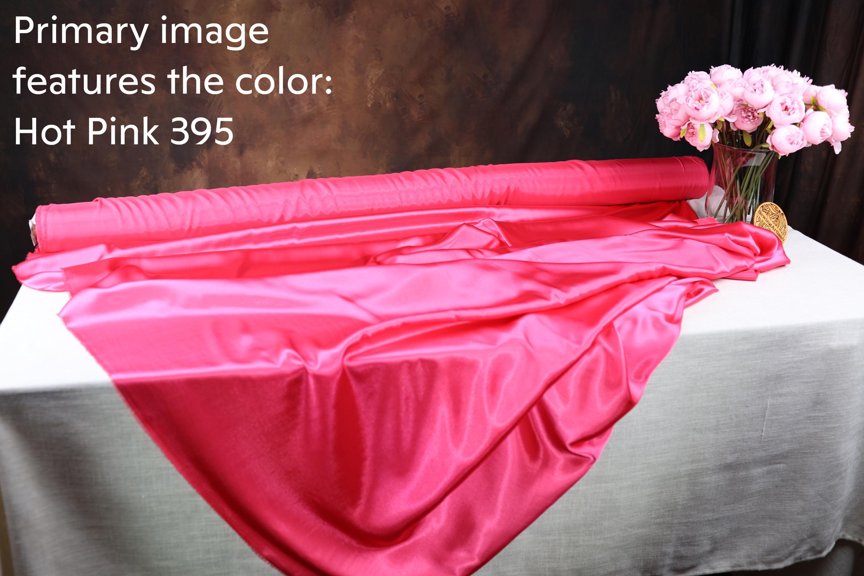 a roll of hot pink satin fabric on a table, with a vase of pink flowers next to it.