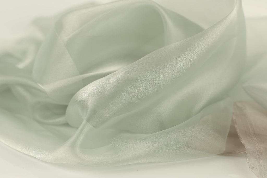 The image is a close-up of a soft, flowing fabric with a pale green color. The fabric appears to be made of silk or a similar material, and it has a smooth, shiny texture. The fabric is crumpled and wrinkled, giving it a delicate and elegant appearance.