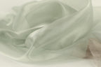 The image is a close-up of a soft, flowing fabric with a pale green color. The fabric appears to be made of silk or a similar material, and it has a smooth, shiny texture. The fabric is crumpled and wrinkled, giving it a delicate and elegant appearance.