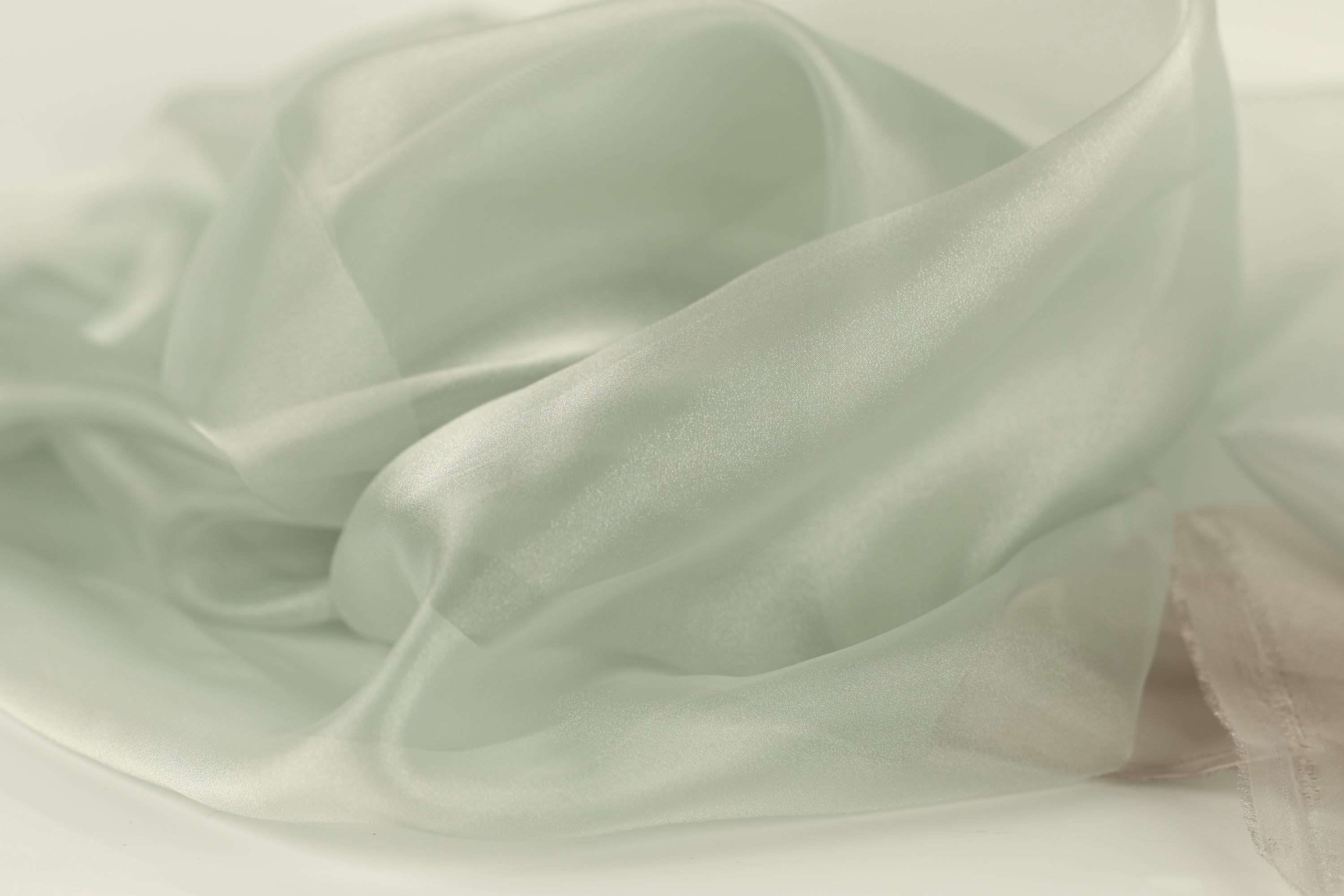 The image is a close-up of a soft, flowing fabric with a pale green color. The fabric appears to be made of silk or a similar material, and it has a smooth, shiny texture. The fabric is crumpled and wrinkled, giving it a delicate and elegant appearance.