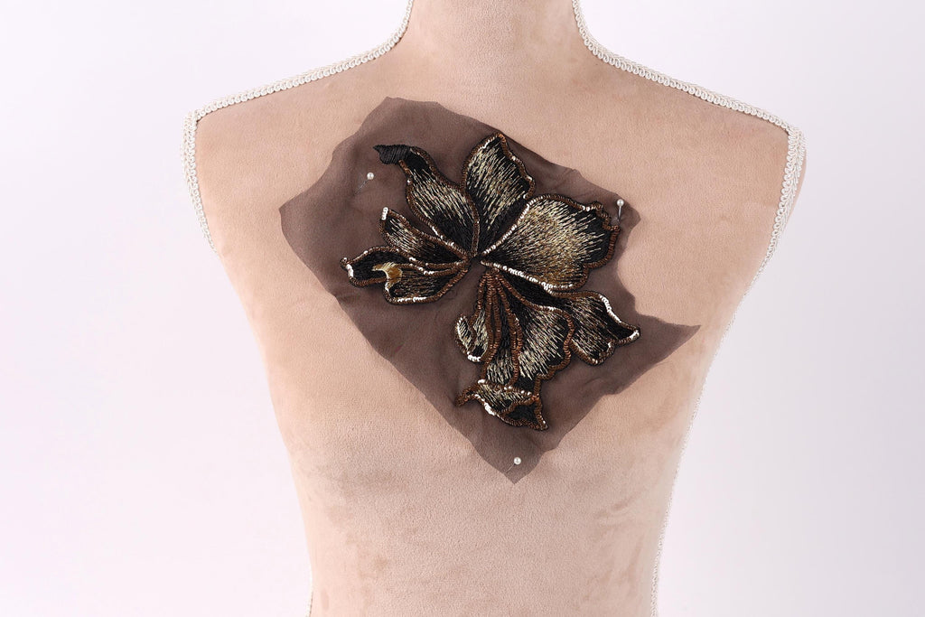 A mannequin torso with a decorative brown fabric piece featuring a black and gold floral pattern on the chest area.