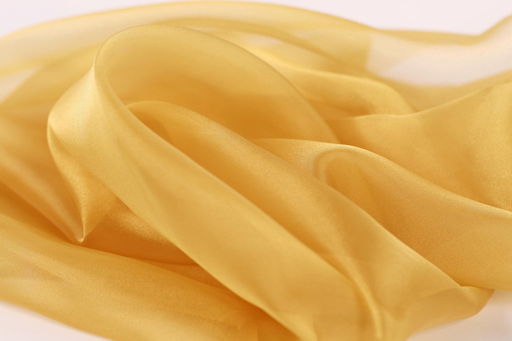 The image is a close-up of a soft, flowing fabric with a golden yellow color. The fabric appears to be made of silk or a similar material, and it has a smooth, shiny texture. The fabric is crumpled and wrinkled, giving it a delicate and elegant appearance.