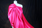 A mannequin wearing a bright pink satin dress with a flowing, draped design.