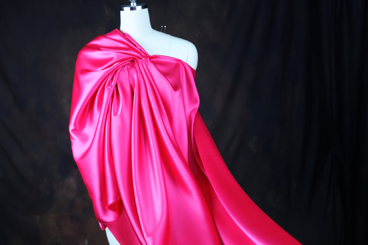 A mannequin wearing a bright pink satin dress with a flowing, draped design.