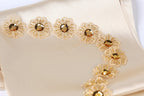 a close-up view of a delicate, beige fabric adorned with a series of small, intricately designed gold flowers. The flowers are arranged in a curved pattern, creating a visually appealing and elegant design.