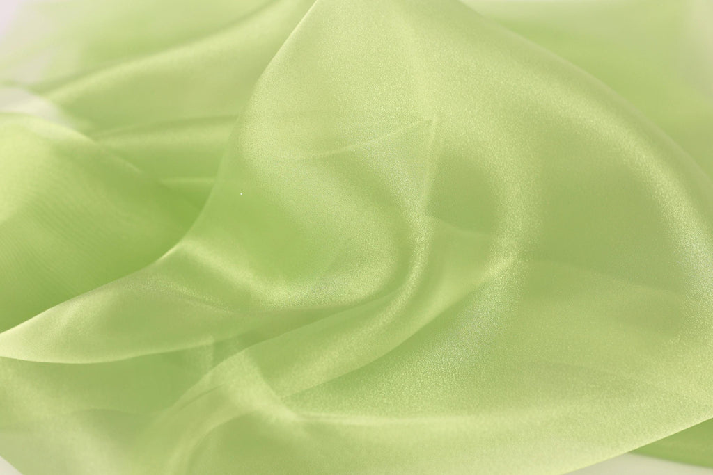 The image is a close-up of a soft, flowing fabric with a pale green color. The fabric appears to be made of silk or a similar material, and it has a smooth, shiny texture. The image does not contain any discernible objects or actions, and it does not depict a scene or a person. The image is a simple, uncluttered composition that focuses on the fabric's texture and color.