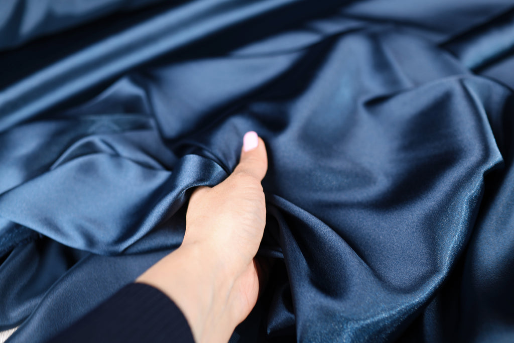 A hand is holding a piece of blue satin fabric, gently touching it.