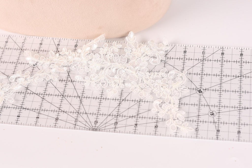 a close-up view of a delicate white lace piece, possibly a veil or a decorative element, placed on a ruler for measurement purposes.