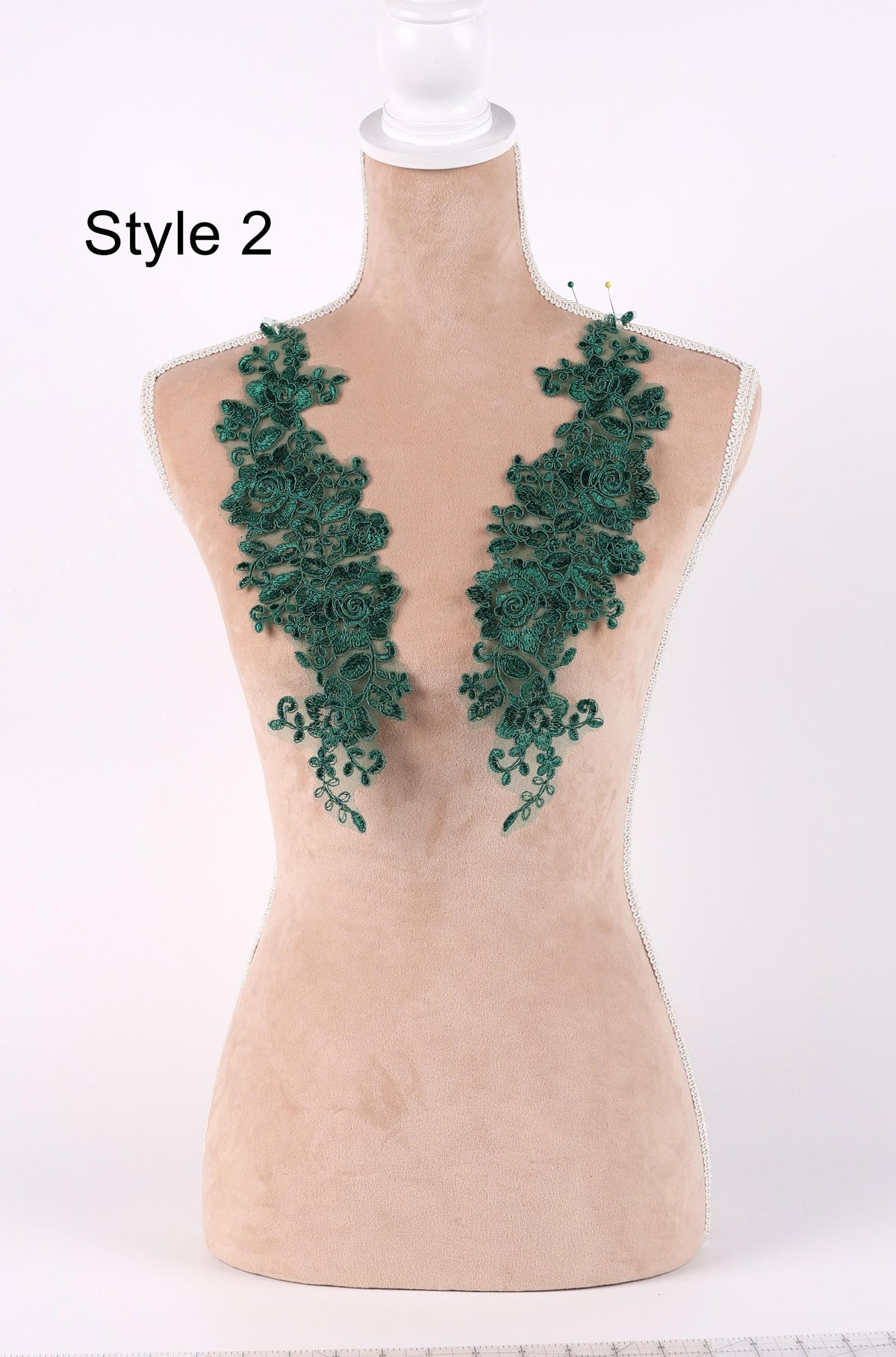 A mannequin wearing a beige dress with green floral embroidered patches on the chest area.