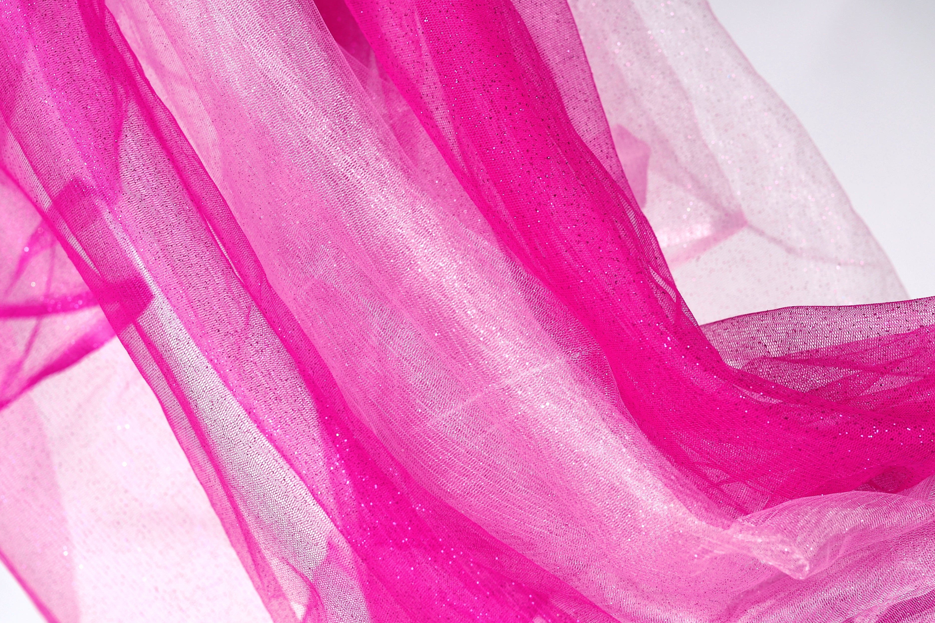 a close-up view of a fabric with a pink and white color scheme, featuring a shiny, sparkly texture.