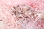 A close-up view of a delicate, pink, and white fabric with a floral pattern, featuring sequins and lace-like details.