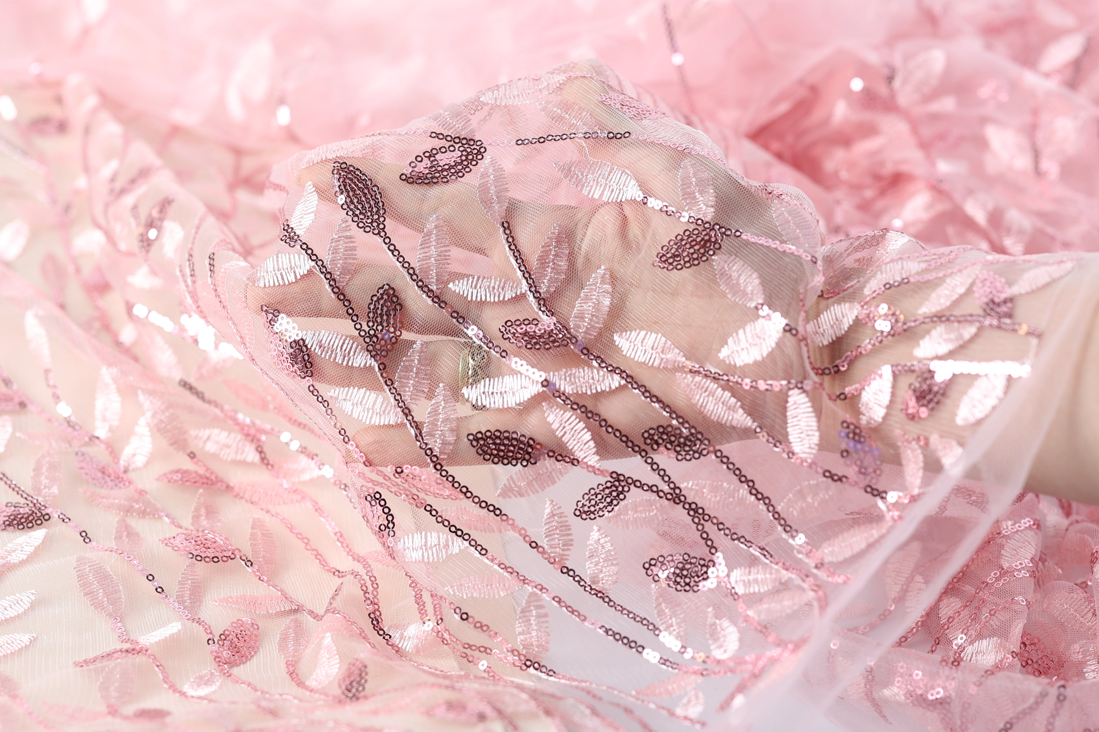 A close-up view of a delicate, pink, and white fabric with a floral pattern, featuring sequins and lace-like details.