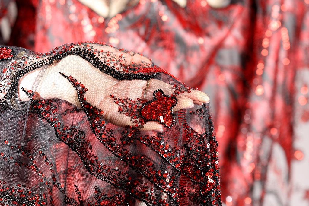 A close-up view of a hand holding a piece of fabric with red sequins and a black lace-like pattern.