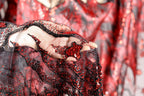A close-up view of a hand holding a piece of fabric with red sequins and a black lace-like pattern.