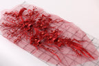 a close-up view of a red floral lace piece with intricate details, including red flowers and beads, placed on a pink background.