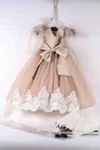 A beige dress with lace trim and a bow detail is displayed on a hanger, accompanied by a lace piece and a pair of scissors.