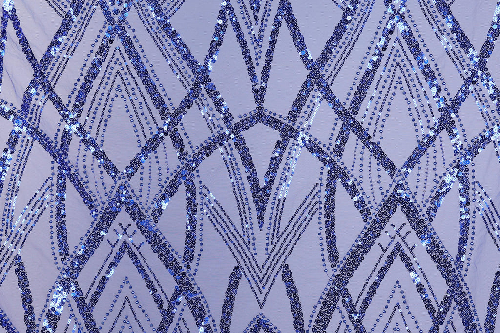 a close-up view of a fabric with a repeating pattern of blue sequin designs. The pattern consists of various diamond shapes and lines, creating a visually striking and intricate design. The fabric appears to be a light purple color, which complements the blue sequin pattern. The image does not contain any text or additional objects, and the focus is solely on the detailed pattern of the sequin design.